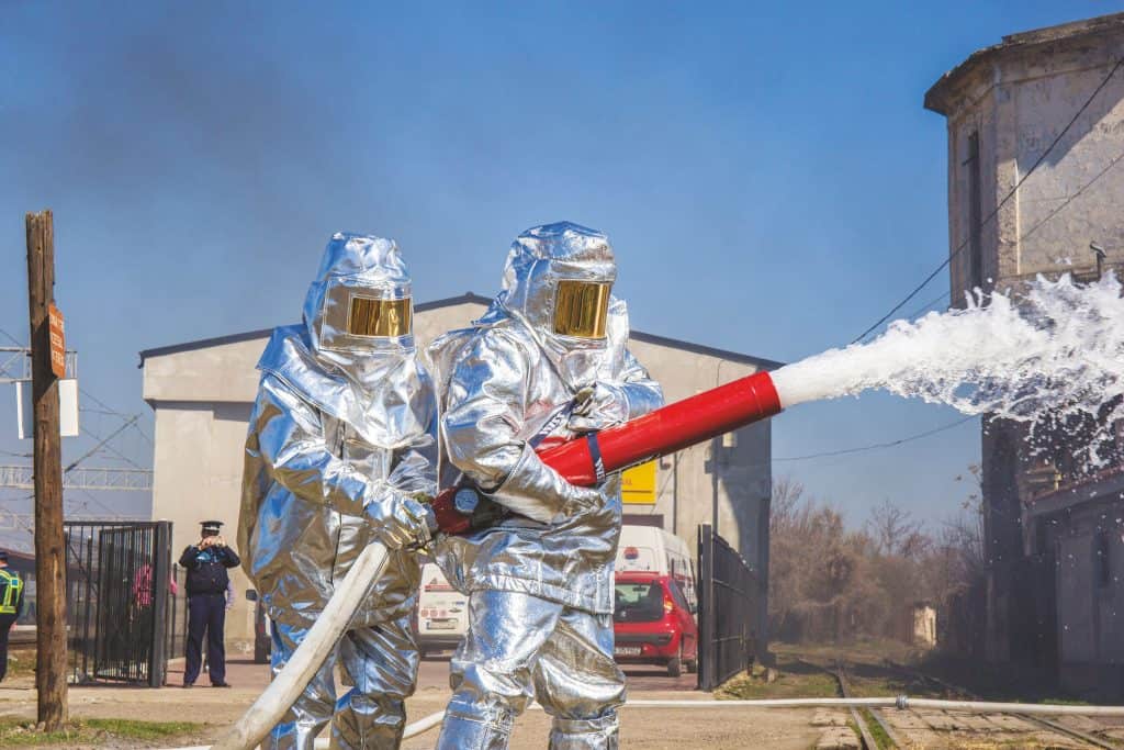 Pompieri (în binom) pregătiți pentru lichidarea unui incendiu, cu utilizarea spumogenului (substanță de stingere hidrocarburi)
